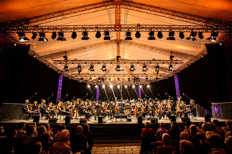 Ein Orchester spielt drau&szlig;en w&auml;hrend ein Publikum zuh&ouml;rt. Es ist nachts.