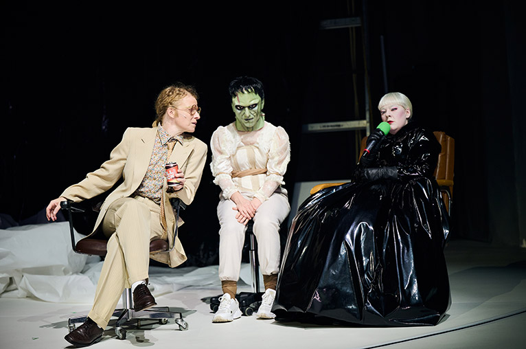 Ein Interview mir Mary Shelley. Neben ihr sitzt jemand mit einer Frankensteinmaske und eine Person im Anzug, die zu ihr guckt.